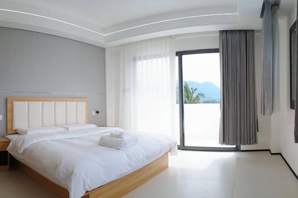 A modern bedroom with a large bed, a sliding glass door to a balcony, and a view of the outdoors.
