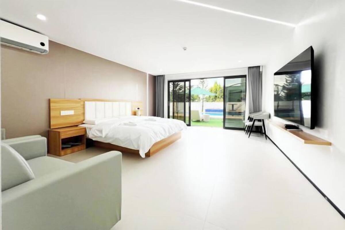 A modern bedroom with a large bed, a TV, and a sliding glass door to a balcony.