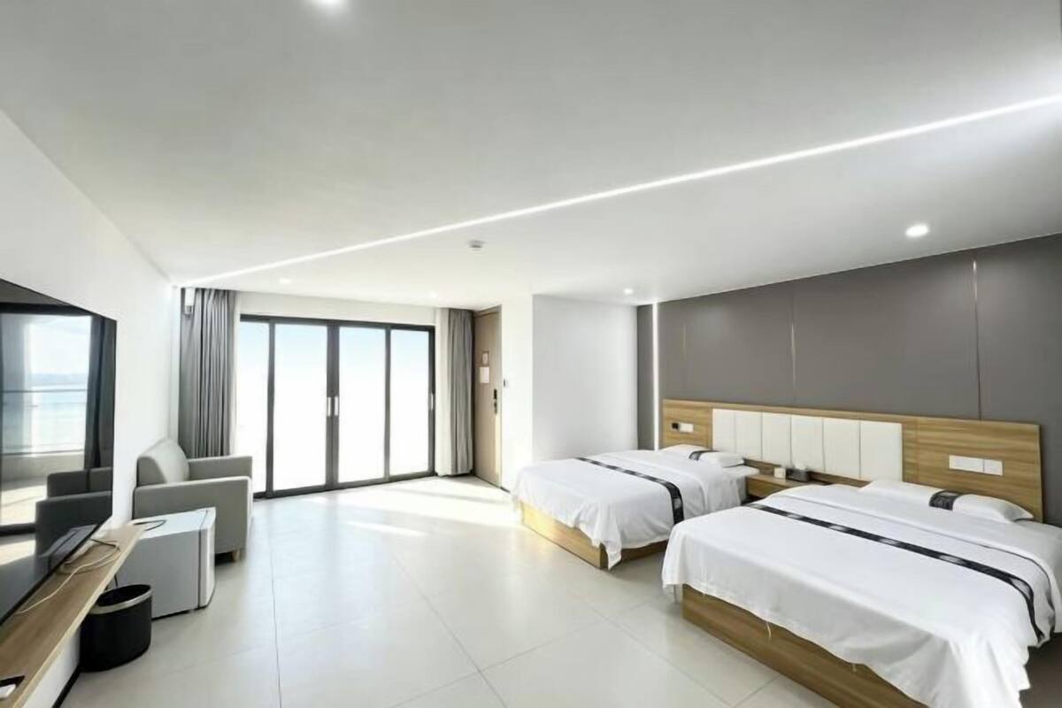A modern hotel room with two beds, a TV, a sofa, and a large window.