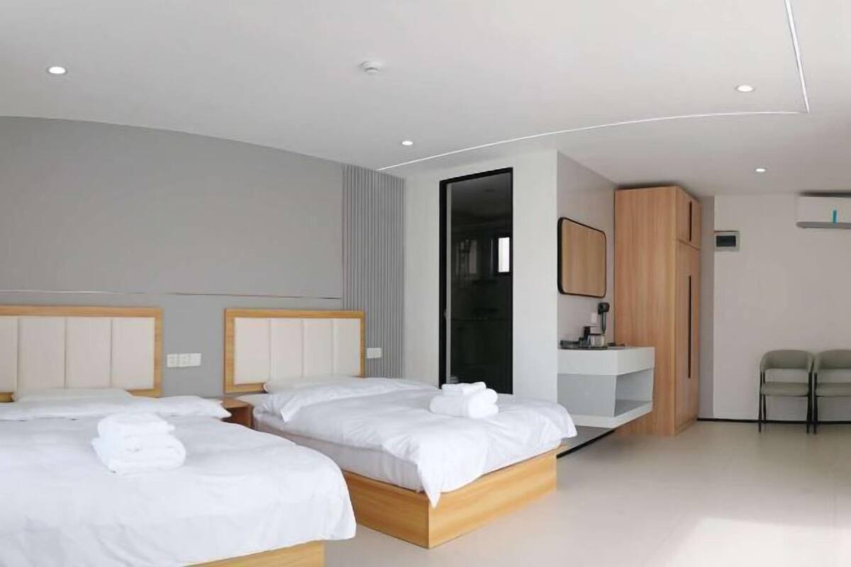 A modern hotel room with two beds, a wooden cabinet, a small desk, and a mirror.