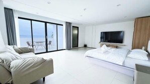 Habitación de hotel moderna con una cama grande, un sofá, un televisor y un balcón con vista al mar.