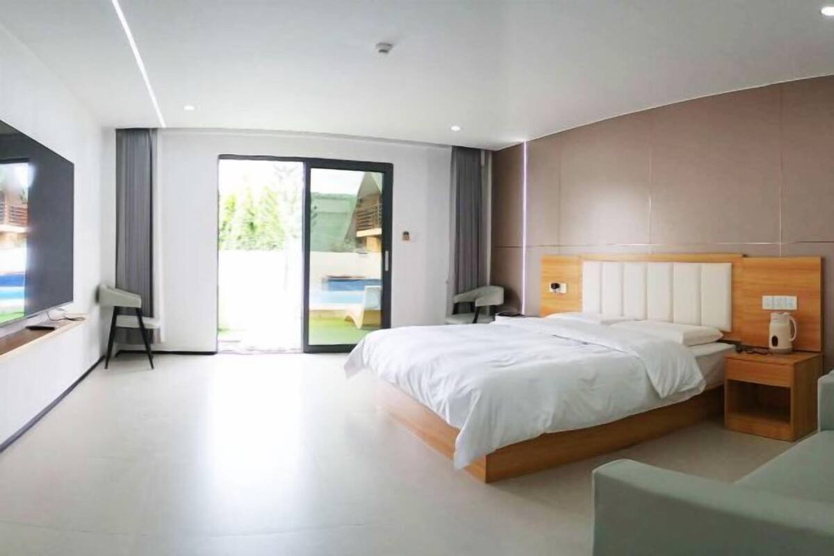 A modern bedroom with a large bed, a TV, and a sliding glass door leading to a balcony.