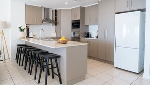A modern kitchen with a central island, bar stools, a refrigerator, and a sink. - Dolce Vita, Esplanade (Aldinga Beach)