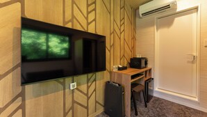A room with a wall-mounted TV, a desk with a computer, a trash bin, and an air conditioning unit. - MAX CUBE Inami Seafront (Inami)