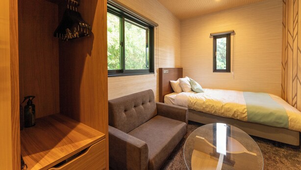 A room with a bed, a sofa, a glass table, and a wardrobe. - MAX CUBE Inami Seafront (Inami)