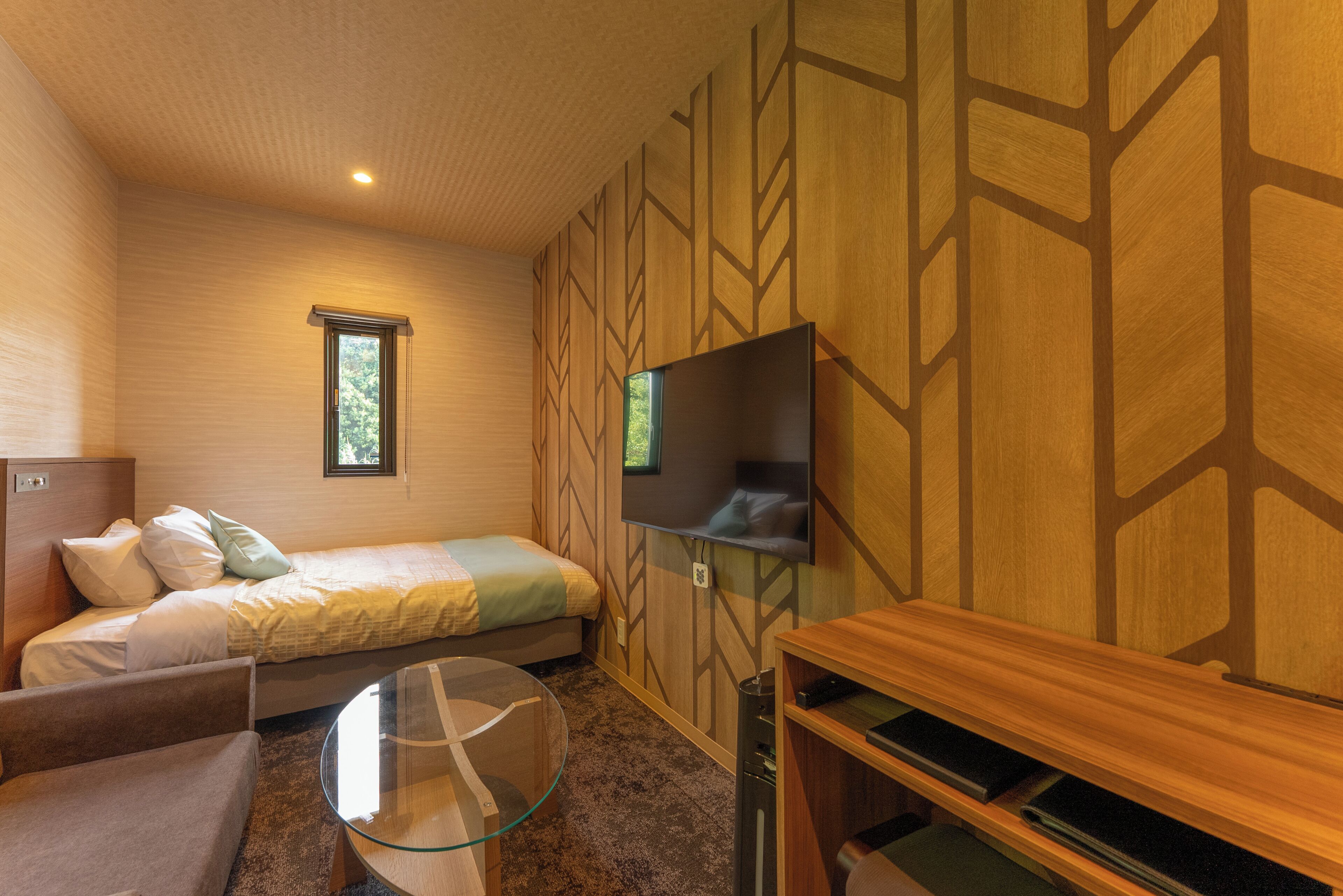 A bedroom with a bed, a TV, a glass table, and a wooden wall design.
