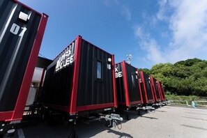 A row of black and red shipping containers with visible text and numbers, parked outdoors. - MAX CUBE Inami Seafront (Inami)
