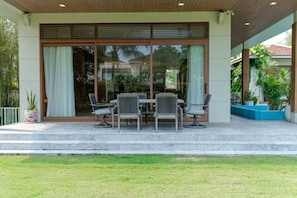 A covered outdoor seating area with a table and chairs, a glass door entrance, and a small garden. - Stunning Luxury Villas with Expansive Grounds: An Unforgettable Experience (Da Nang)