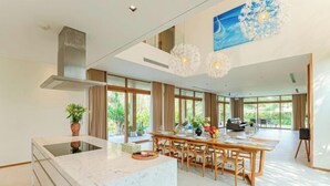 A spacious kitchen with a central island, large windows, and a dining area with a wooden table and chairs. - Stunning Luxury Villas with Expansive Grounds: An Unforgettable Experience (Da Nang)