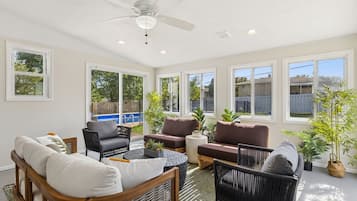A sunlit patio with a ceiling fan, large windows, and outdoor seating.