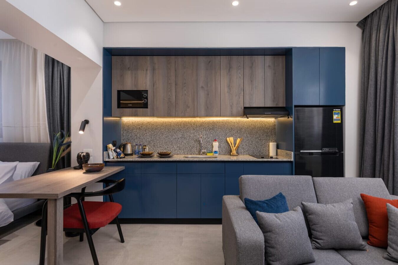 Une cuisine moderne avec des meubles bleus, un four encastré et un réfrigérateur noir.