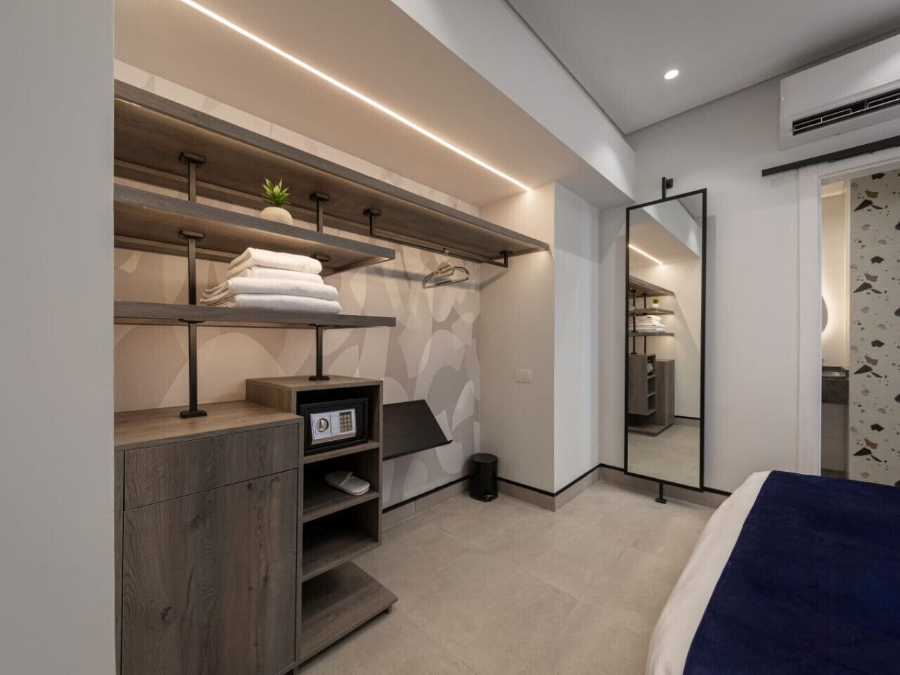 A modern bedroom with a bed, a built-in wardrobe, a mirror, and a small plant.