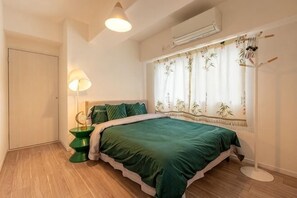 Quarto com cama, luminária de cabeceira, radiador e janela com cortinas.