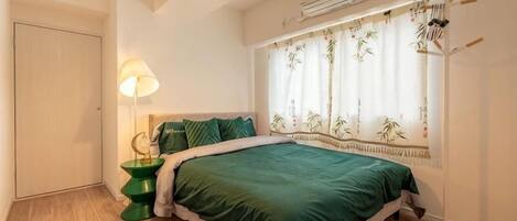 A bedroom with a bed, a bedside lamp, a window with curtains, and a radiator.