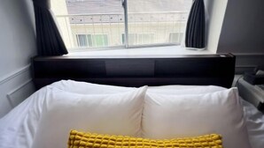 A hotel room with a bed, white pillows, a window with curtains, and a view of buildings outside. - Ikebukuro No`3 (Tokyo)