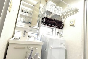 Un baño con lavamanos blanco, espejo y barra para toallas. Hay repisas sobre el lavamanos con cestas y toallas.