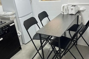 Una cocina compacta con encimera gris, sillas negras, un tostador y una tetera.