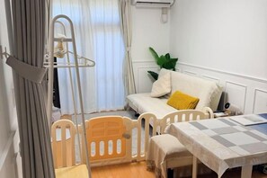 A small, cozy room with a bed, a table, and a chair. There is a window with curtains, a plant, and a hanging light fixture. - Ikebukuro No`3 (Tokyo)