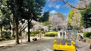 A playground with yellow equipment, a small building, and trees with green foliage. - Ikebukuro No`3 (Tokyo)