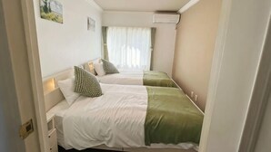 A room with two beds, a window with curtains, an air conditioning unit, and a wall-mounted light fixture. - Ikebukuro No`3 (Tokyo)