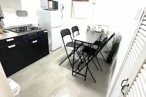 A compact kitchen with a gas stove, dishwasher, and white refrigerator. There is a dining table with four chairs and a potted plant. - Ikebukuro No`3 (Tokyo)