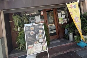 L’entrée d’un restaurant, avec un panneau affichant le menu, des plantes en pot et une banderole jaune.