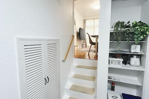 A staircase leading to a room with a white door and a shelf with plants and a clock. - Ikebukuro No`3 (Tokyo)