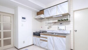 Una cucina compatta con piano cottura integrato, lavello e microonde. Si apre una porta a sinistra e una porta bianca a destra.