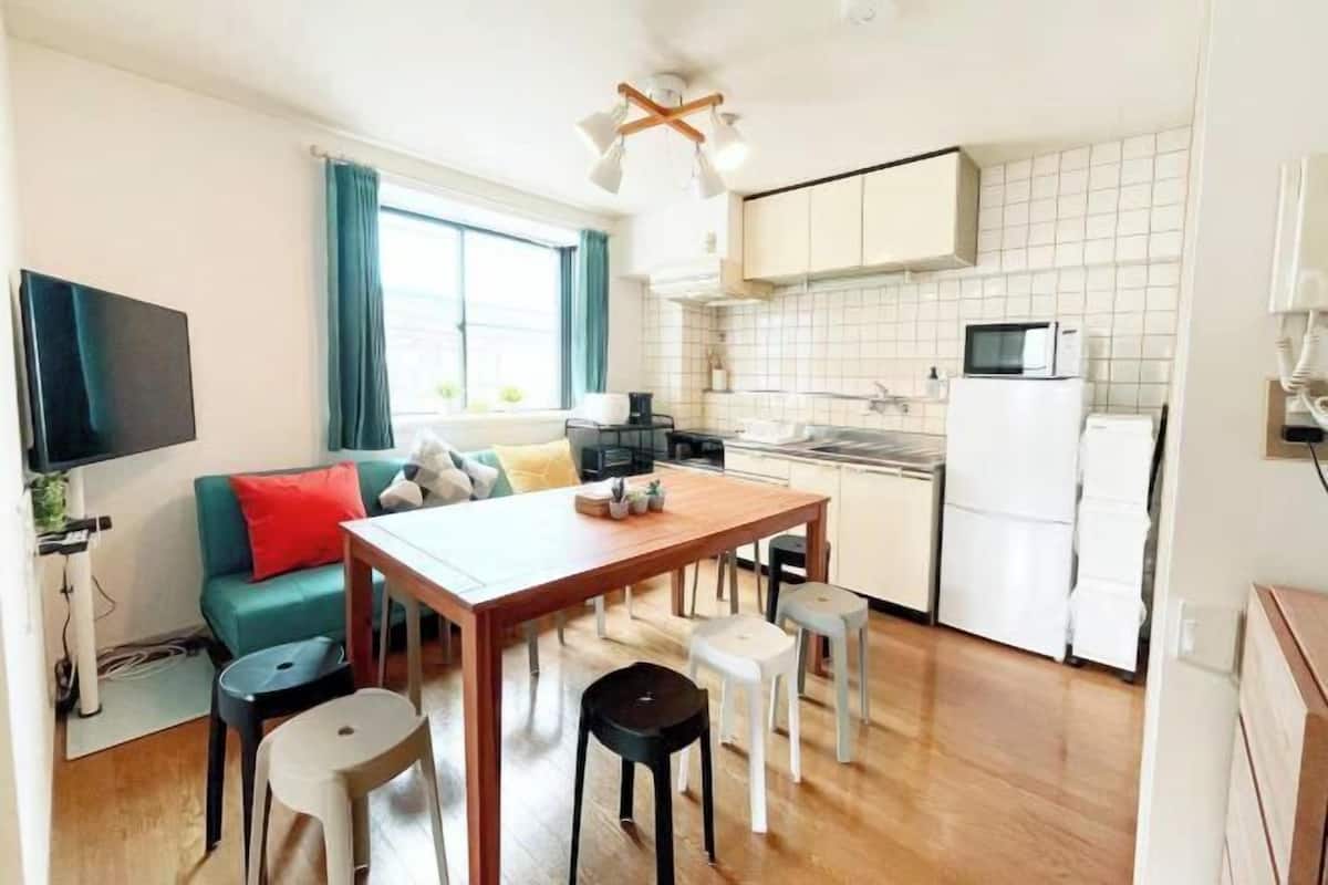 Un espacio habitable compacto con kitchenette, comedor y zona de estar con sofá y sillas.