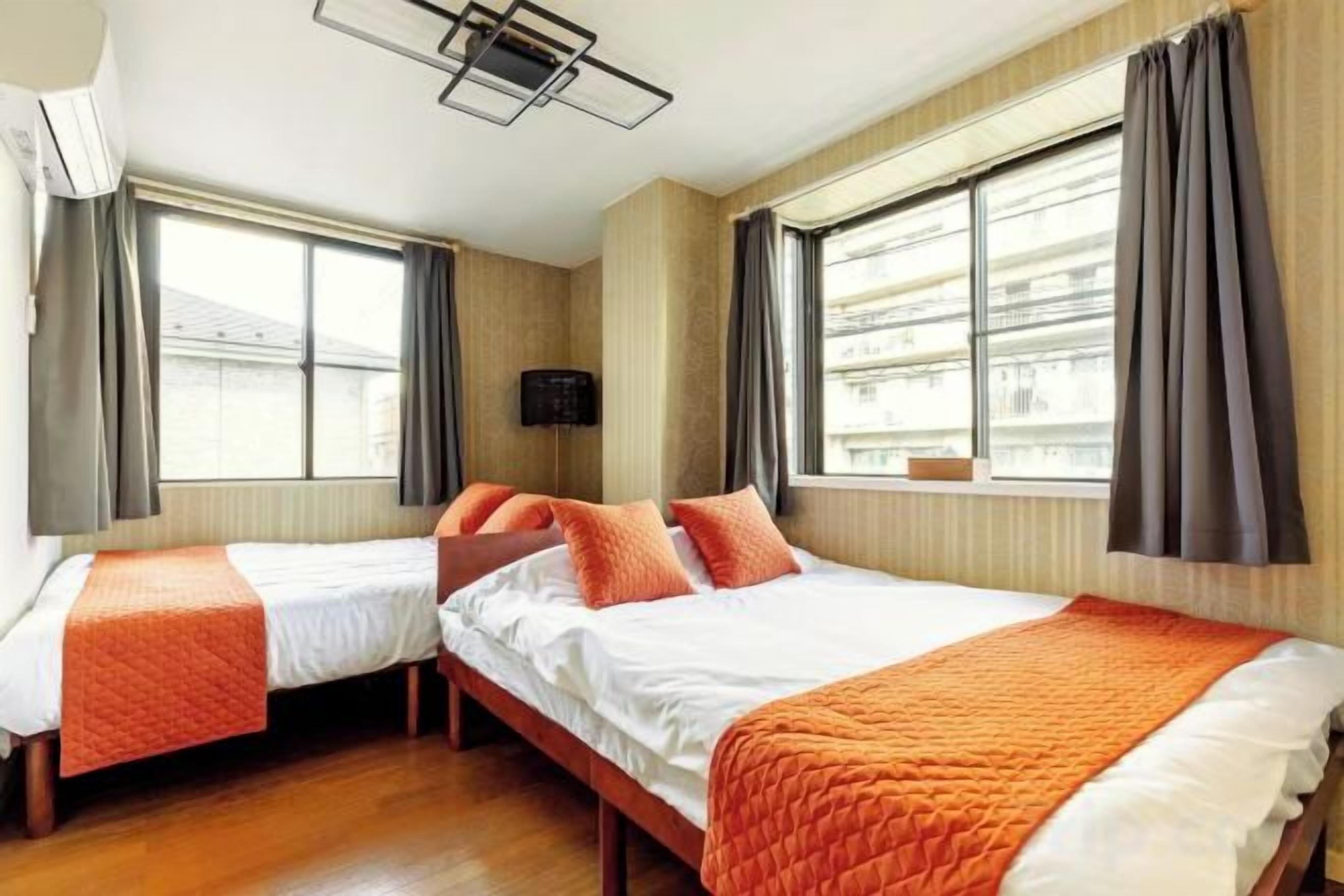 A hotel room with two beds, a flat-screen TV, and large windows with curtains.