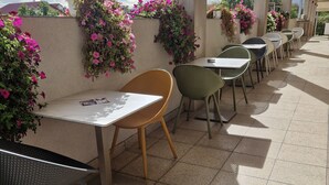 Um café ao ar livre com mesas e cadeiras, rodeado por paredes decoradas com plantas floridas.