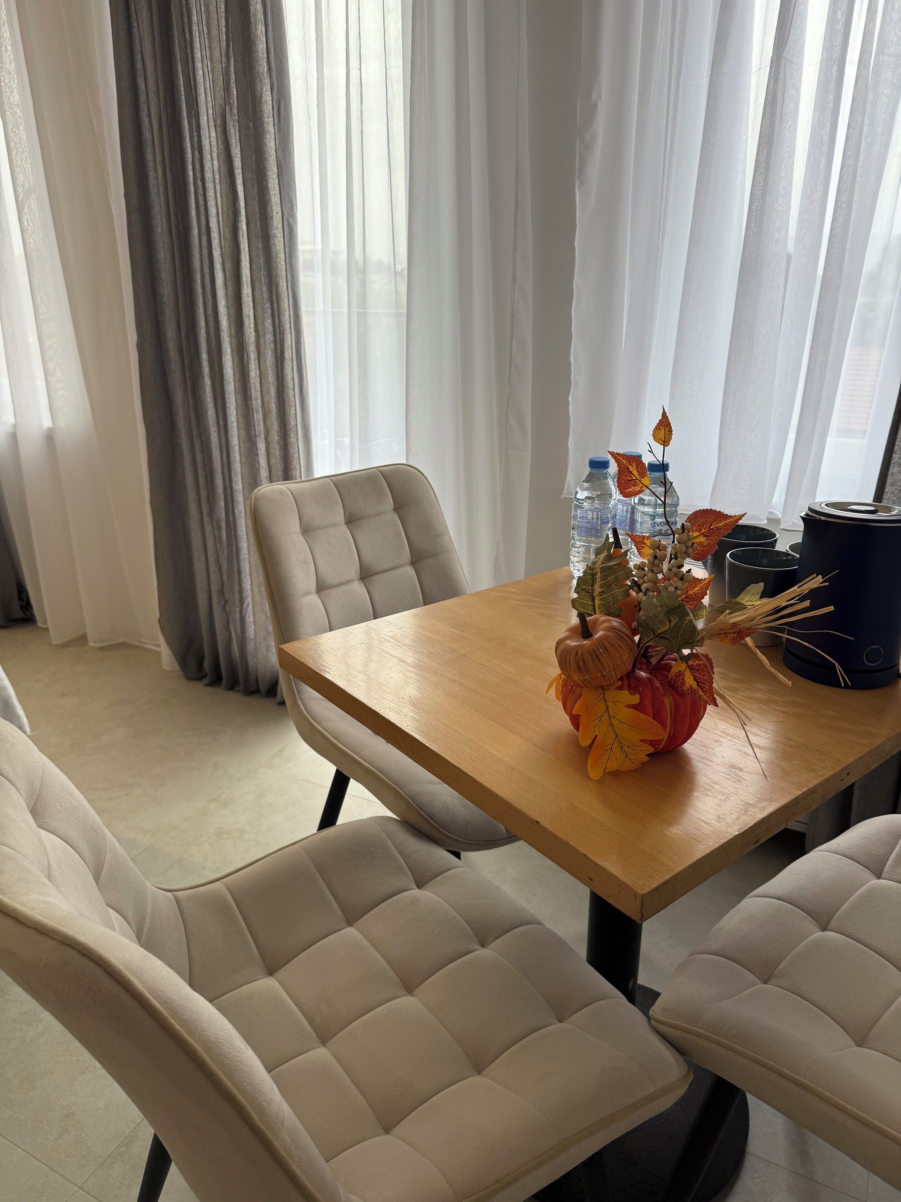 A dining area with a wooden table, beige cushioned chairs, and a vase with decorative elements.