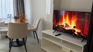 Uma sala de estar moderna com uma televisão de tela plana em um suporte branco, lareira, mesa de jantar com cadeiras e janela com cortinas.