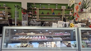 Vitrine de pastelaria com diversos doces e balcão de café com chávenas e máquina de café.