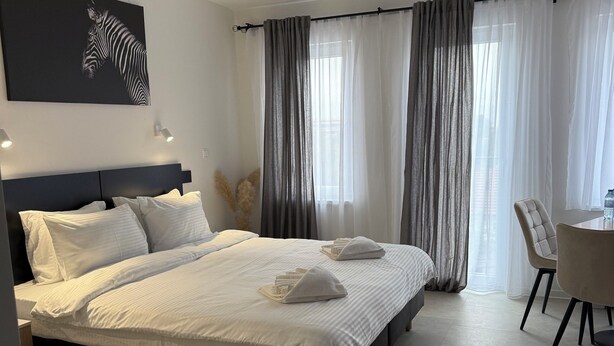 Quarto de hotel com duas camas, área de refeições e uma janela grande com cortinas.