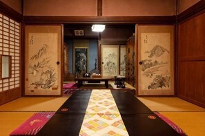 A traditional Japanese room with tatami flooring, sliding doors with artwork, and a low table with a hanging scroll. - [Kao HOUSE Jakusui-an] 100-year-old traditional Japanese house stay (Katori)