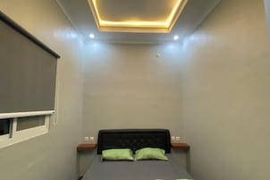 Un dormitorio pequeño y moderno con cama, almohadas verdes, ventana con persianas e iluminación empotrada en el techo.