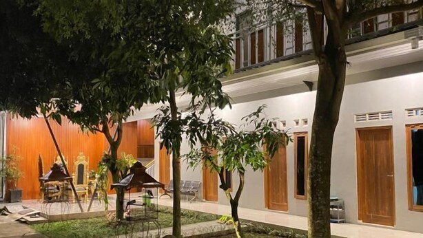 Une cour bordée d’arbres, un petit jardin et un bâtiment doté de portes et de fenêtres en bois.