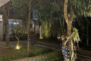 Un espacio al aire libre de noche con árboles, una calle y un edificio con cerca ornamentada.