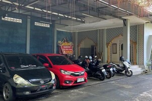 Un edificio con un vestíbulo cubierto, un coche rojo y varias motocicletas estacionadas afuera.