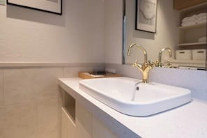 A modern bathroom with a white sink, gold faucets, and a framed picture on the wall.