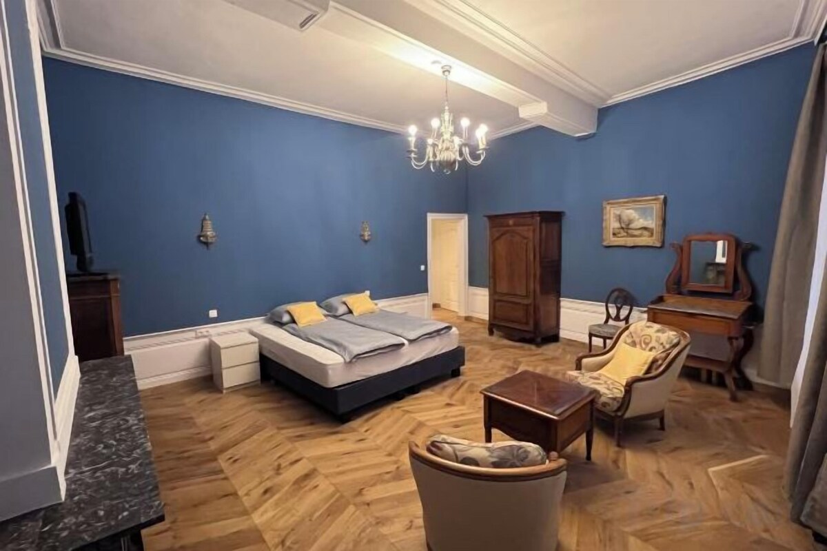 A bedroom with a bed, a chair, a desk, and a chandelier.