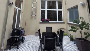 Een binnenplaats met betegelde vloer, een tafel met stoelen, een barbecue en een potplant.