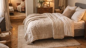 Een slaapkamer met een houten vloer, een bed met een sprei, een nachtkastje met een lamp, een stoel en een schilderij aan de muur.
