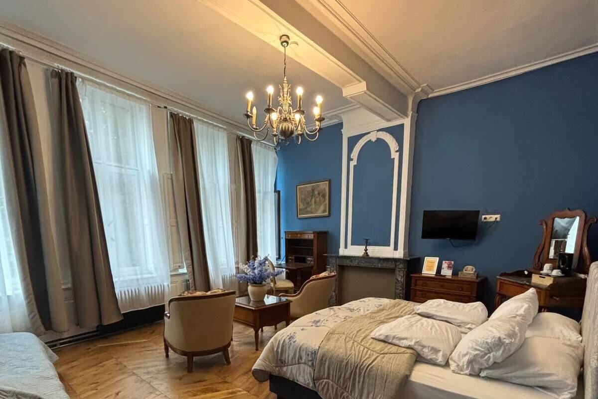A hotel room with a large bed, a desk, a chair, a television, and a fireplace.