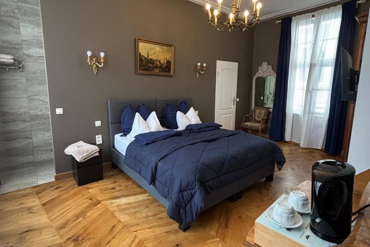 A bedroom with a bed, a chandelier, a painting, and a coffee maker.