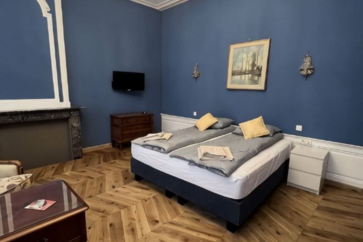 A bedroom with a double bed, a flat-screen TV, a fireplace, and a painting on the wall.