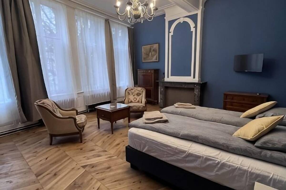 A room with a bed, a chair, a small table, a fireplace, and a TV.