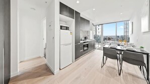 Eine moderne Küche mit Kühlschrank, Mikrowelle und Herd, ein Essbereich mit Tisch und Stühlen sowie große Fenster mit Blick auf die Stadt.