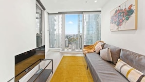 Ein modernes Wohnzimmer mit einer Couch, einem gelben Teppich und einem großen Fenster mit Blick auf die Stadt.